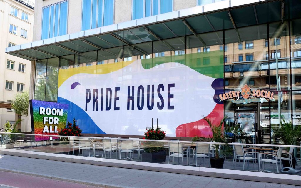 En vägg på Clarion Hotel Stockholm är täckt utav en färgglad reklamskylt för Pride House. Till vänster syns en regnbågsfärgad skylt "room for all"