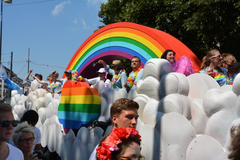 Ett ekipage i en Pride parad. Det är en solig dag och flera regnbågsflaggor syns i bilden. Fotot är taget utav Jesper Hansén.