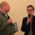 Nicke Johansson och Helena Westin stående med var sin mikrofon i handen. Nicke står till vänster och håller i ett plakat. Helena har mikrofonen lyft till munnen. Fotot är från 2014 och taget av Jon Voss.
